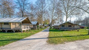 Un chemin de gravier mène à une rangée de maisons mobiles dotées de vérandas attenantes, le tout étant entouré d’arbres.