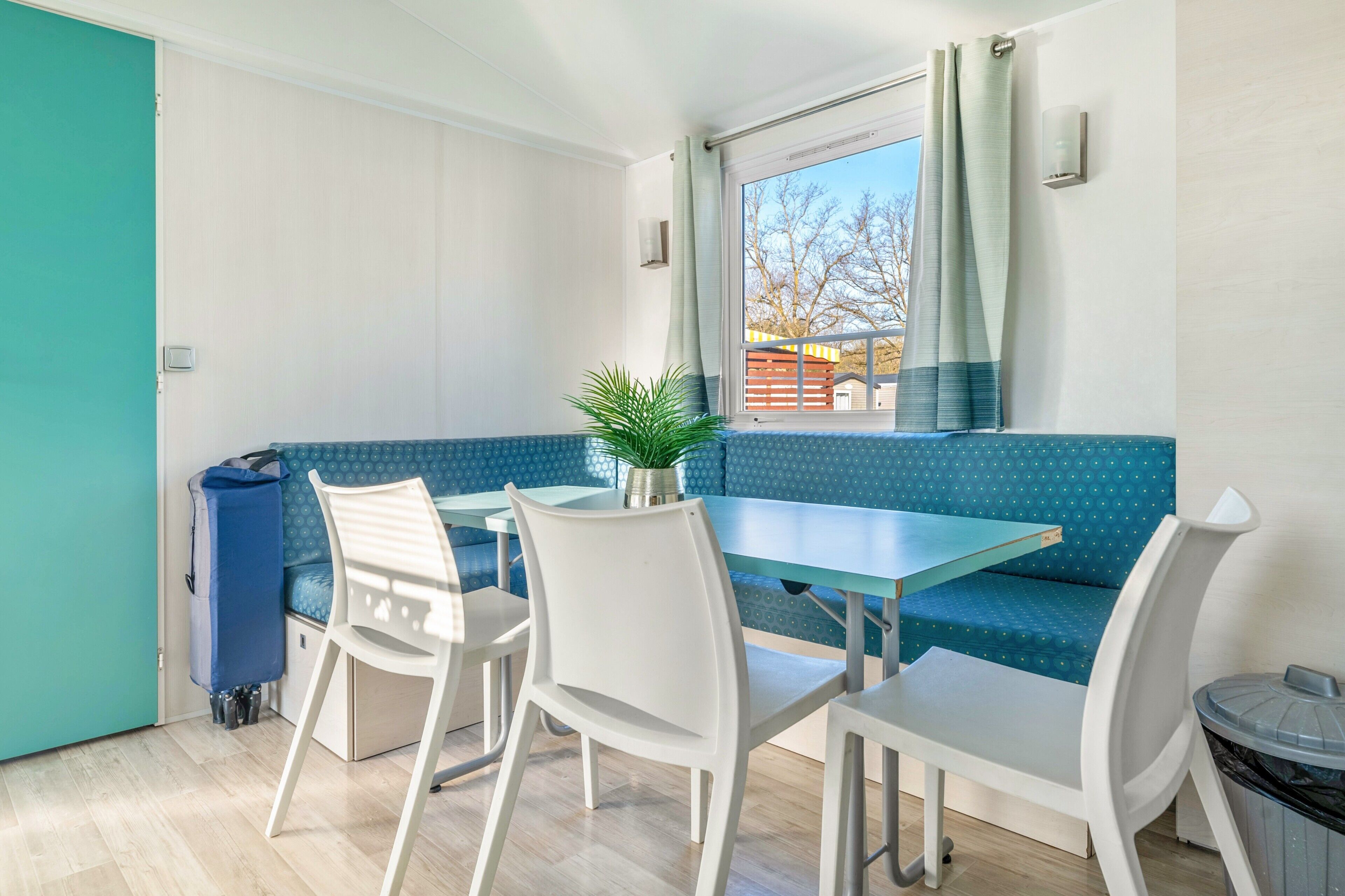 A room with a blue sofa, white chairs, a small table, and a window with curtains.