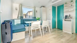 Un espace de vie compact comprenant un canapé, une table à manger, des chaises, un petit coin cuisine et une armoire.