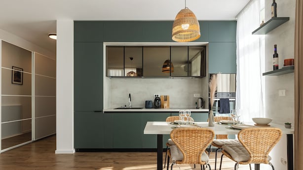 Una cocina moderna con encimera blanca, sillas de mimbre y una lámpara colgante.
