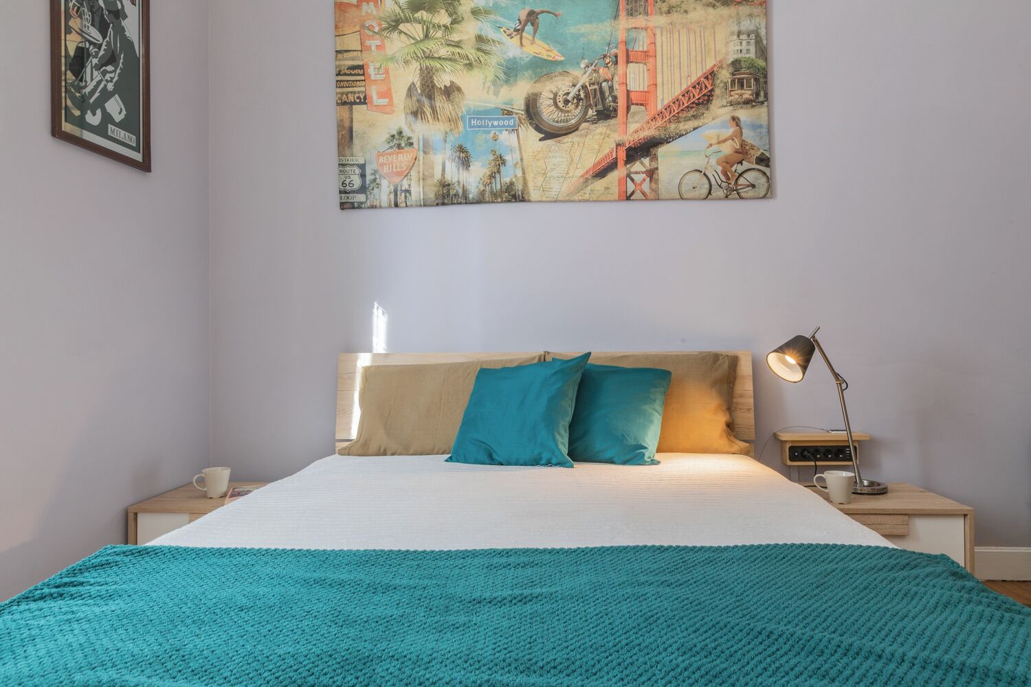 Een slaapkamer met een bed, nachtkastje, lamp en een schilderij aan de muur.