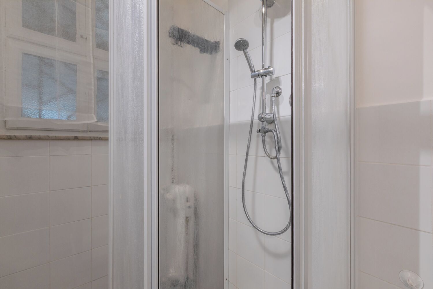 Ducha envuelta en vidrio, con cabezal de ducha de mano y manguera flexible.