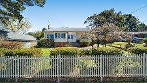A single-story house with a front yard, a picket fence, and a car parked in the driveway.