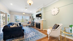 A living room with a fireplace, a large clock, and a television.