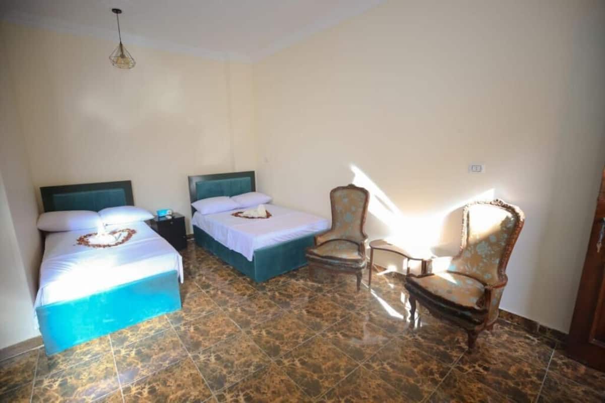 A room with two beds, a chair, and a small table.