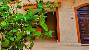 A courtyard with a building featuring multiple windows with decorative grills, a tiled roof, and a large door. - Great Pyramid View Inn (Giza)