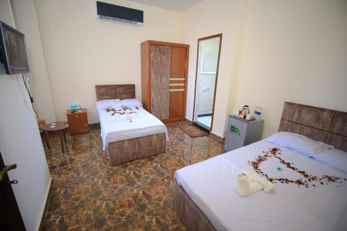 A hotel room with two beds, a wardrobe, a small table, and a desk with a chair.
