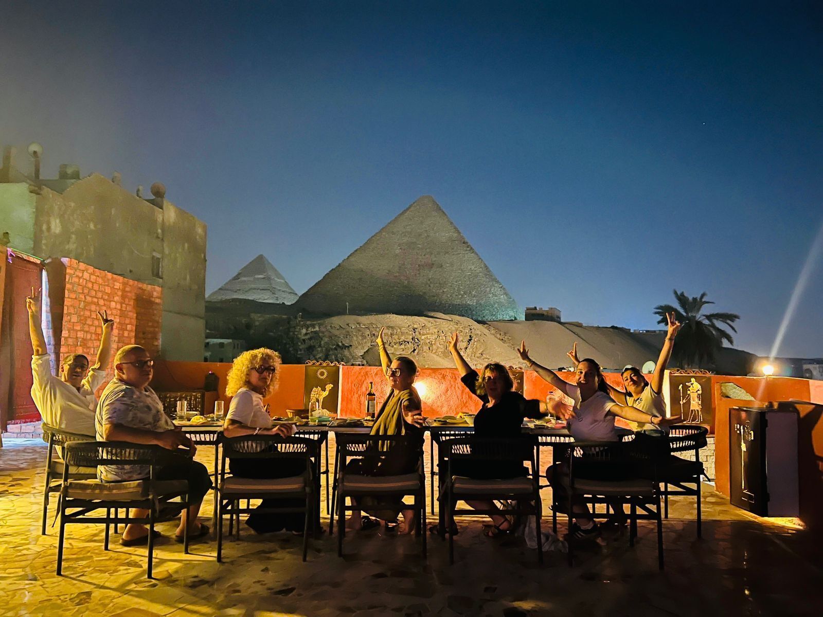 Un grupo de personas cenando al aire libre, con una pirámide al fondo.
