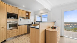 A modern kitchen with wooden cabinets, stainless steel appliances, and a view of the countryside through a large window. - Jamburra - Breathtaking views of the Blue Mountains! (Leura)