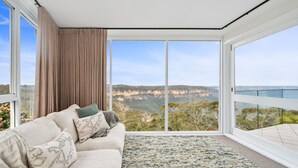 A modern living room with a large sliding glass door leading to a balcony with a scenic view of cliffs and greenery. - Jamburra - Breathtaking views of the Blue Mountains! (Leura)