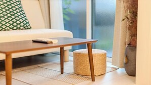 Una habitació amb un sofà, una taula de fusta, un tamboret trenat i un finestral gran.