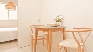 Habitació minimalista amb una taula de fusta, dues cadires, una petita planta en test i un llum penjant.