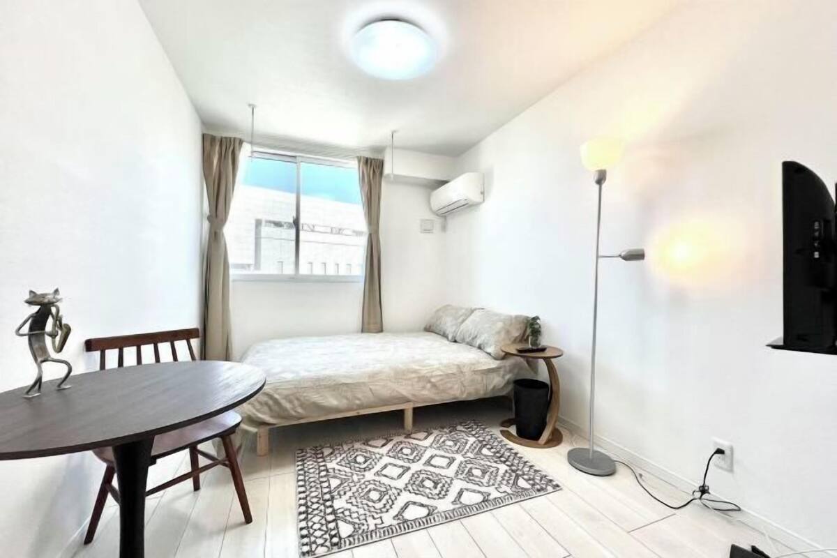 Una habitación pequeña y bien iluminada con una cama, una mesa y una alfombra estampada.