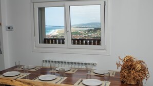 Mesa de comedor para seis personas con vista a la playa y al pueblo a través de una ventana.