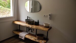 Un baño con tocador de madera, un espejo redondo, un lavamanos y un perchero para toallas.