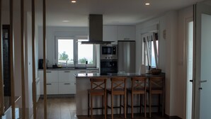 Una cocina moderna con una isla central, sillas de madera, electrodomésticos de acero inoxidable y vistas al exterior.