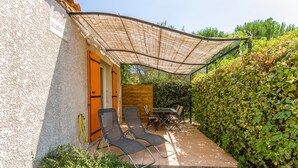 Eine Terrasse mit zwei Liegestühlen, einem Tisch und einem überdachten Bereich mit einem Schild, auf dem 'LE CHENEUVERT' steht.
