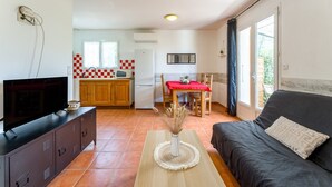 Ein gemütlicher Wohnraum mit Fernseher, Sofa, Esstisch, Küchenzeile und Blick durch eine Schiebetür.