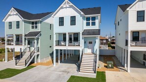 A row of two-story beach houses with balconies, a concrete driveway, and a clear blue sky. - Walk To The Beach! Pet Friendly! (Kill Devil Hills)