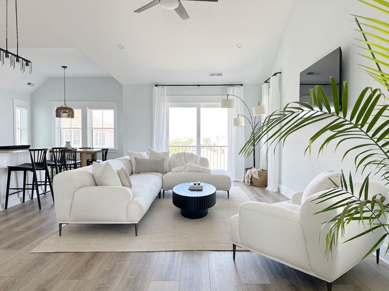 A spacious living room with a white sofa, a round coffee table, and a dining area with chairs and a table.