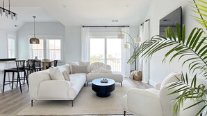 A spacious living room with a white sofa, a round coffee table, and a dining area with chairs and a table. - Walk To The Beach! Pet Friendly! (Kill Devil Hills)