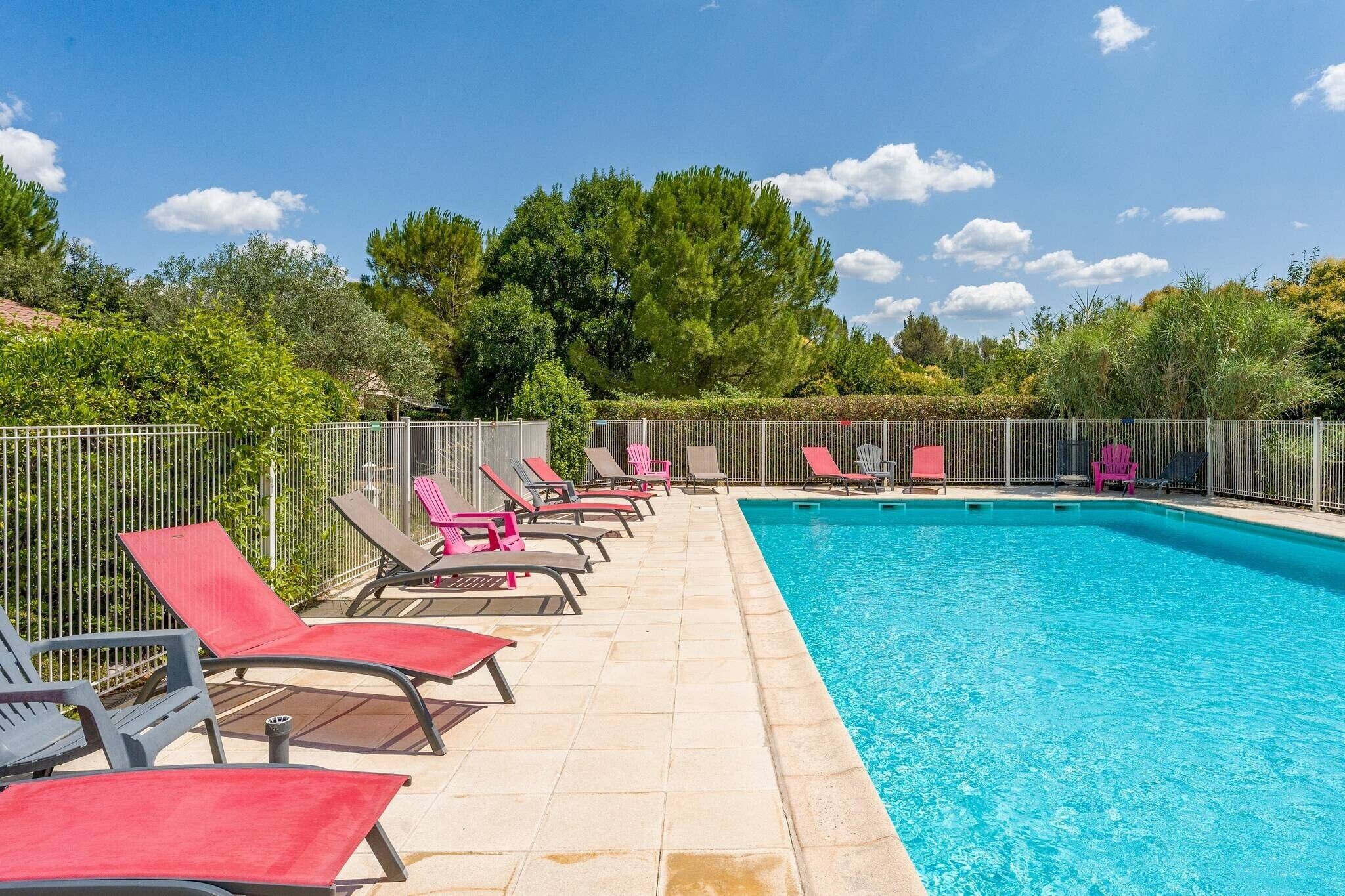 A swimming pool with lounge chairs, surrounded by a fence and trees.