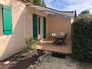 Un petit bâtiment doté d’une terrasse carrelée, d’une table avec des chaises et d’une porte avec des volets verts.