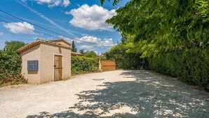 A gravel driveway leading to a small building with a door and window, surrounded by greenery and a clear sky.