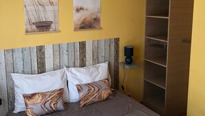 A bedroom with a bed, two pillows, a wooden headboard, a wall-mounted shelf, and a wardrobe.