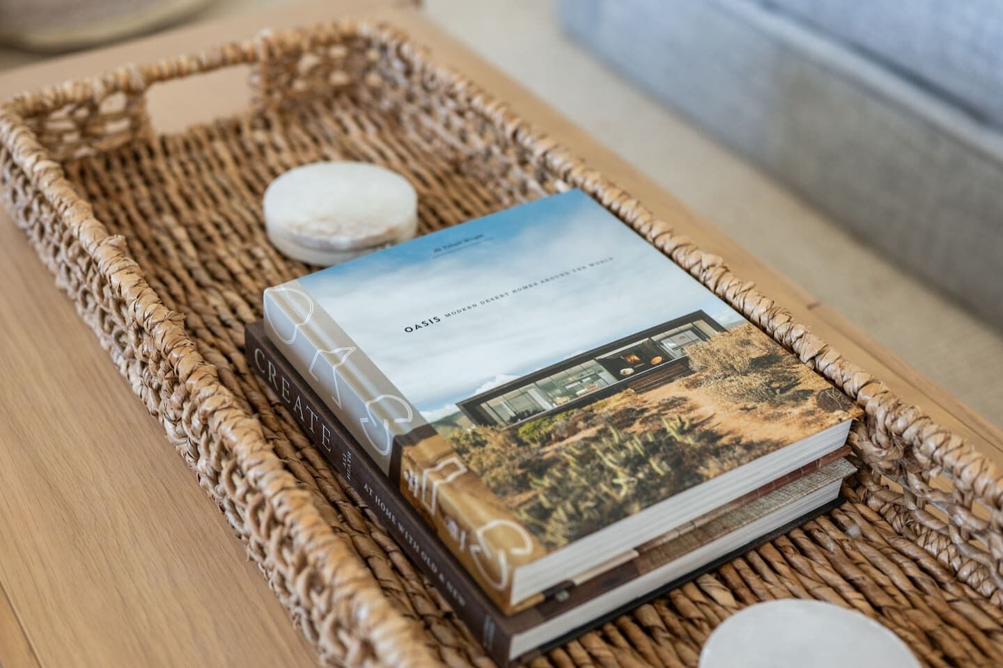 A woven tray with a book titled 'Oasis Modern Desert Homes Around the World' and a small white object.