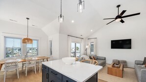 Eine moderne Küche mit Kochinsel, Essbereich mit Stühlen, einer Couch und einem Deckenventilator.