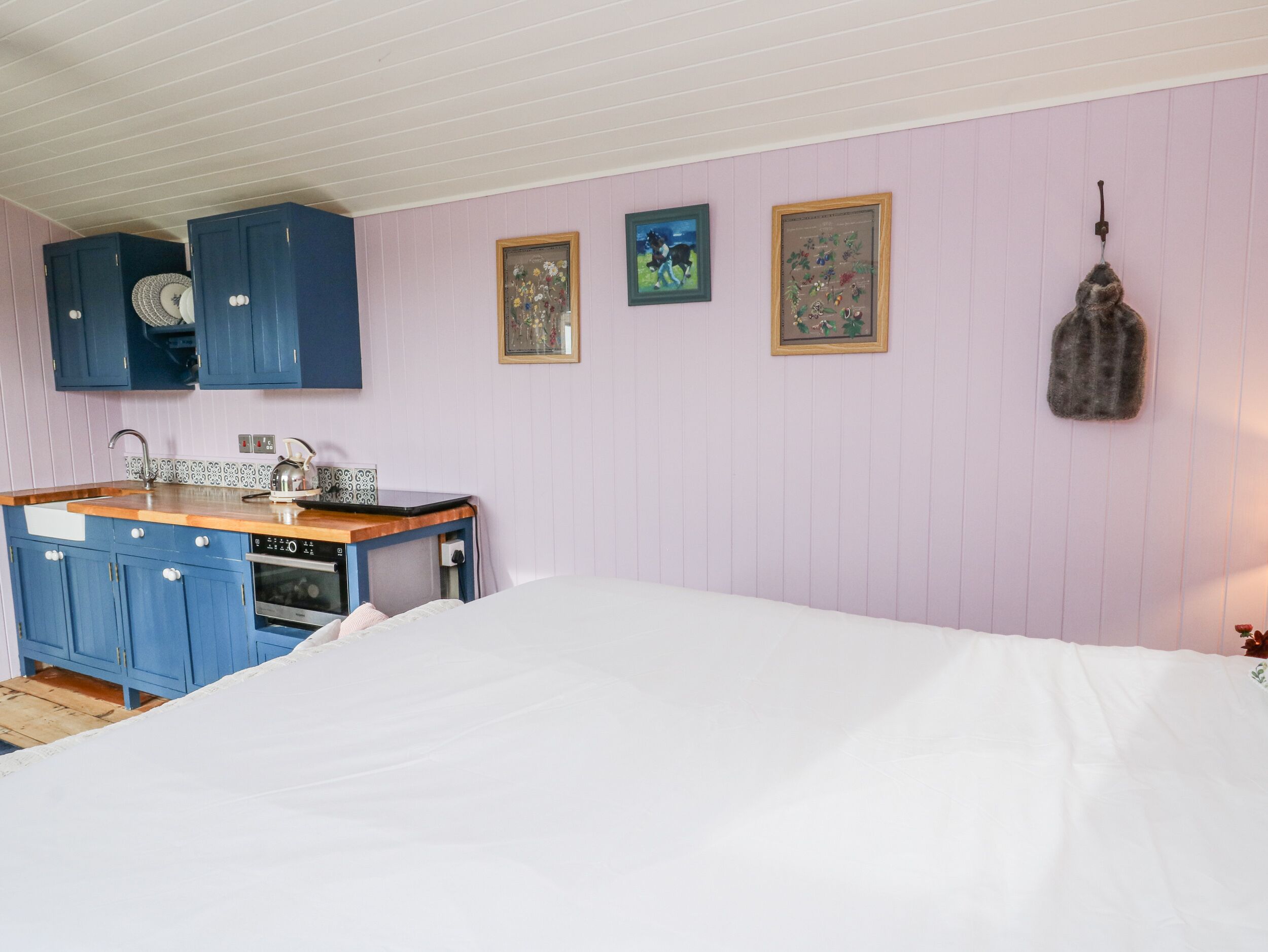 Quarto com cama, uma kitchenette pequena com armários azuis, pia e fogão. Há três quadros na parede.