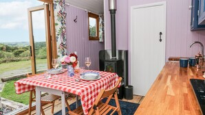 A cozy dining area with a checkered tablecloth, a wooden bench, and a view of the countryside. - Brondel Luxury Shepherd's Hut (Aberystwyth)