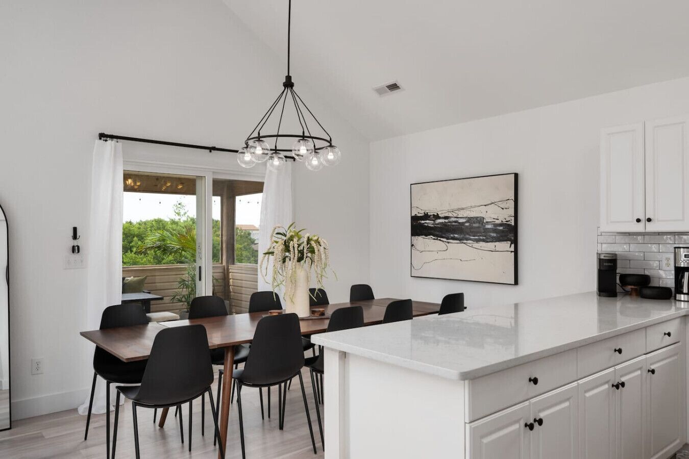 A modern kitchen with white cabinets, a large island, and a dining area with a table and chairs.