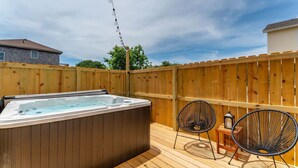 A wooden deck with a hot tub, two chairs, and a lantern.