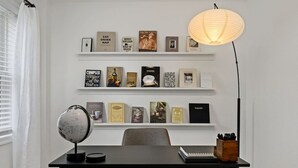 A modern room with a desk, shelves with books, a globe, and a lamp.