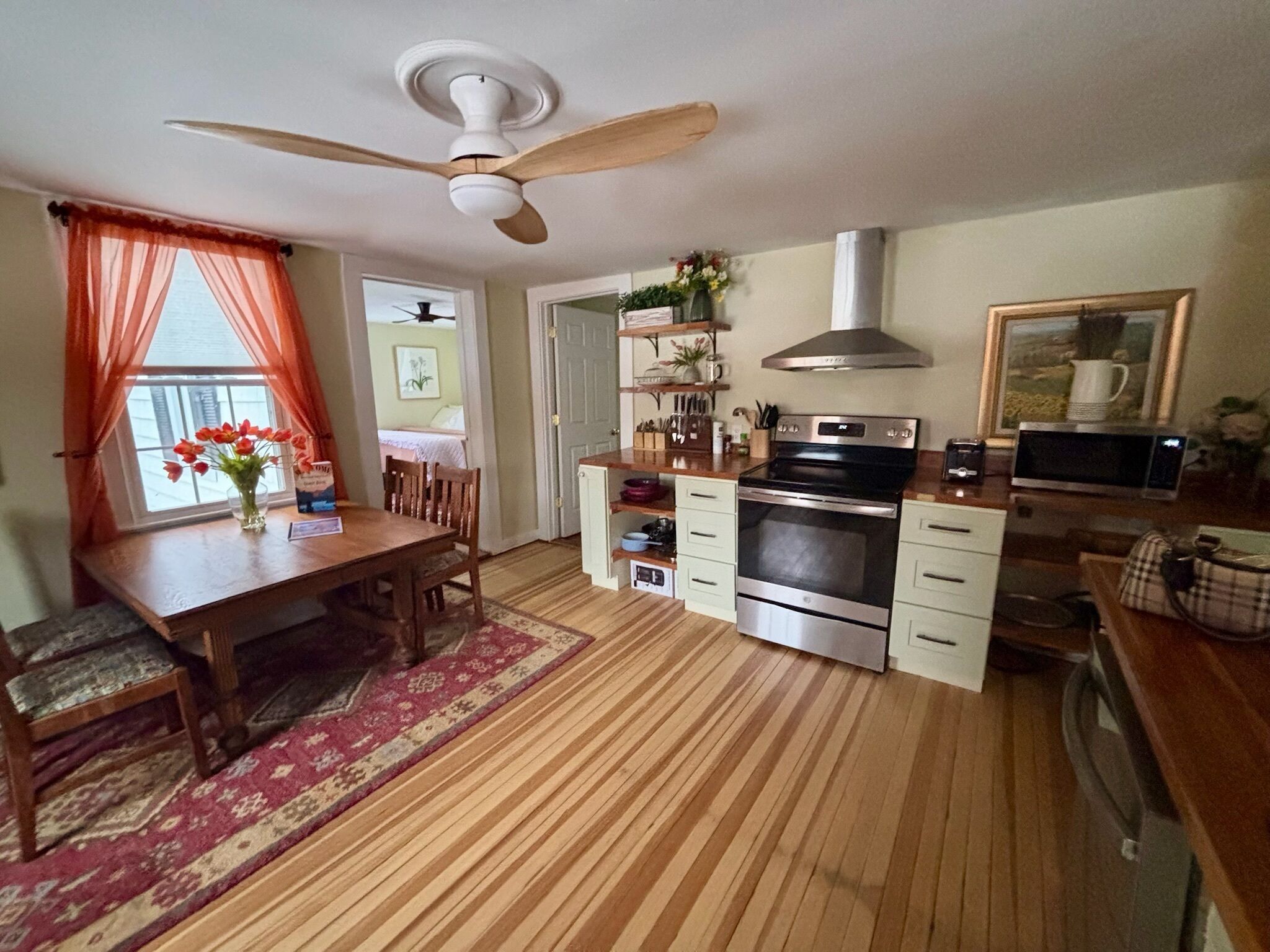 Una cocina con piso de madera, una mesa de comedor con sillas, un ventilador de techo, una estufa y un microondas.