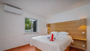 A bedroom with a bed, a window, an air conditioning unit, and a wooden headboard. - Holiday Home 'Valentina' with Shared Pool, Wi-Fi and Air Conditioning (Carvoeiro)