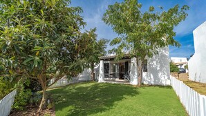 A white building with a covered patio, surrounded by a white fence, and a well-maintained lawn. - Holiday Home 'Valentina' with Shared Pool, Wi-Fi and Air Conditioning (Carvoeiro)