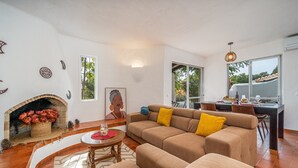 A living room with a fireplace, sofa, and dining area. - Holiday Home 'Valentina' with Shared Pool, Wi-Fi and Air Conditioning (Carvoeiro)