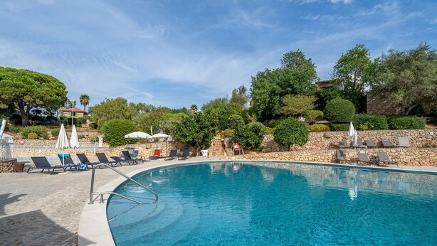A clear blue pool with lounge chairs and umbrellas, surrounded by stone walls and greenery. - Holiday Home 'Valentina' with Shared Pool, Wi-Fi and Air Conditioning (Carvoeiro)