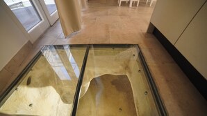 A glass floor in a room with tiled flooring and a door in the background. - Giusy House (Ostuni)