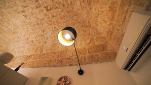 A room with a stone ceiling, a wall-mounted light fixture, a decorative plate, and an air conditioning unit. - Giusy House (Ostuni)