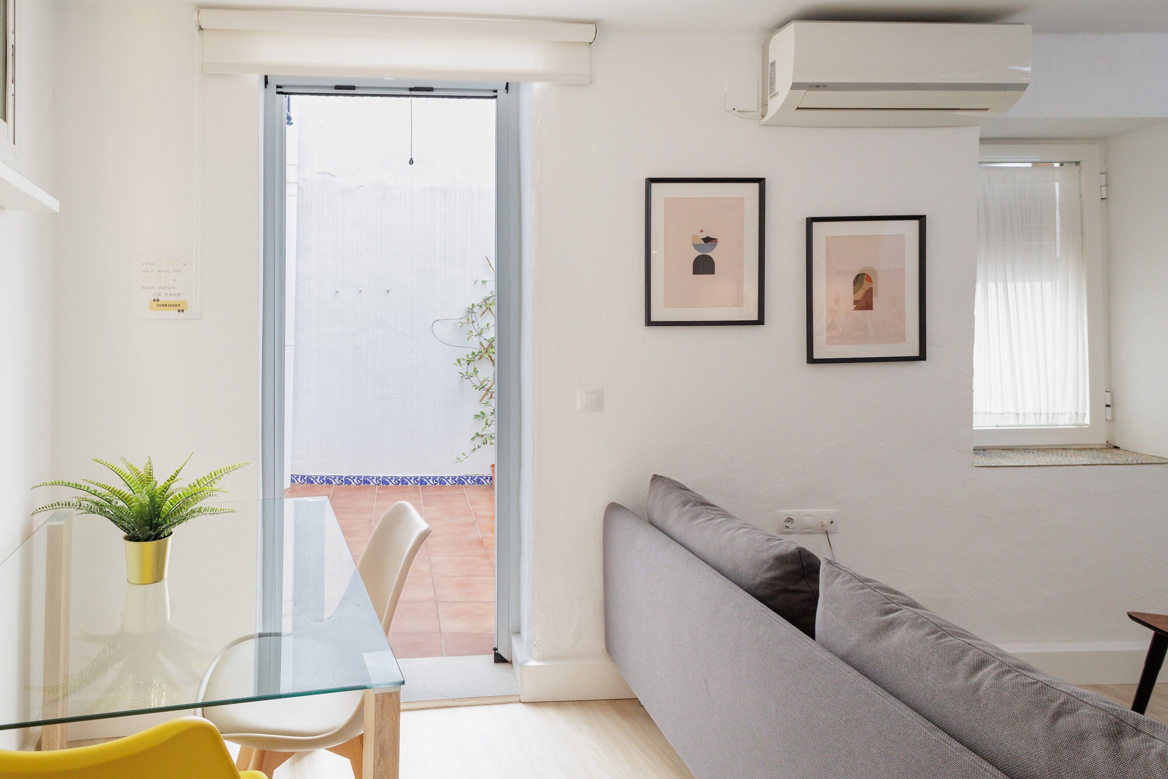 Een moderne woonkamer met een glazen tafel, een grijze bank en twee ingelijste kunstwerken aan de muur.