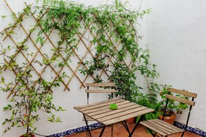 A wooden table and chairs set against a white wall with a climbing plant.