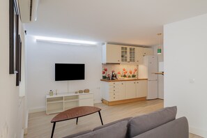 A compact living space with a flat-screen TV, a kitchenette, a sofa, and a small table.
