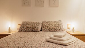 A neatly made bed with floral-patterned pillows, a bedside lamp, and three line drawings on the wall.