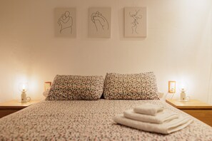 A neatly made bed with floral-patterned pillows, a bedside lamp, and three line drawings on the wall.