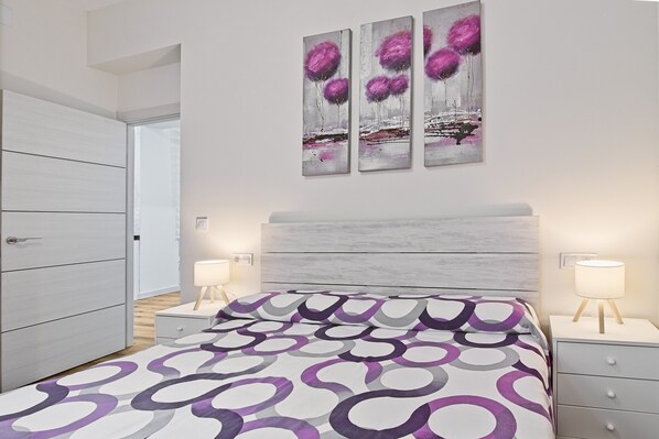 Un dormitorio moderno con cama, mesitas de noche, cómoda y cuadros en la pared.