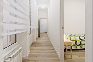 Un pasillo estrecho con un radiador, una puerta al final y una cama con colcha verde y blanca.